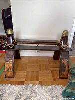 Full view of wood camel saddle showing both legs and decorative carvings, with taped brass knobs on top