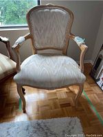 Full front view of the wood framed upholstered chair with carved floral details on armrests and backrest, showing the light beige upholstery and blond wood finish