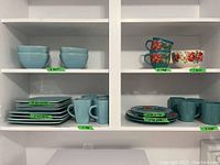Shelves with two distinct sets of dishes labeled with quantities: light blue set on left side including plates, mugs, and bowls; floral patterned dishes and mugs on right side.
