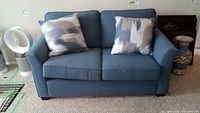 Front view of blue loveseat with two abstract decorative pillows placed on seat cushions.