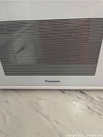 Close-up of Panasonic logo on microwave door showing white exterior and black vent area.