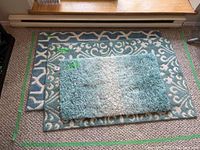 Photo showing all three scatter rugs stacked on a carpeted floor in front of a baseboard heater. Shows size tags on rugs.