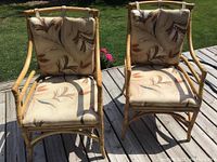 Front view of two bamboo easy chairs on wooden deck in daylight. Both have beige cushions with leaf pattern.