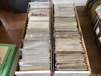 Two cardboard boxes filled with rows of bagged and boarded comic books sorted into categories.