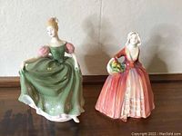 Two Royal Doulton porcelain female figurines side by side on a table, showing full front and side views.