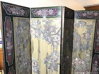 Front view of the four-panel room divider showing painted floral design on gold background with black frame and decorative accents.