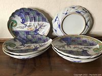 Set of six scalloped edge Imari porcelain plates stacked, showing front decorations with blue, green, purple, and gold floral and geometric designs.