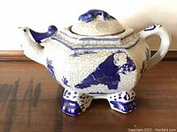 Front side of the rectangular ceramic teapot showing panda playing with a ball and a bird forming the spout; white with blue crackle glaze and paw feet