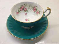 Teacup sitting on saucer showing the floral inside and blue exterior with gold trim.