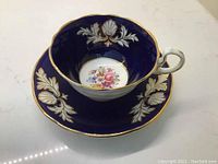 Perspective of cup sitting inside the saucer showing blue and gold leaf design with floral bouquet inside cup and saucer centers.