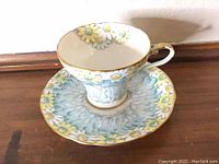 Front view of teacup placed on saucer showing floral chrysanthemum and daisy pattern with gold trim