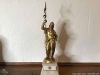 Full view of bronze soldier statue on white marble base showing entire figure and flagpole.