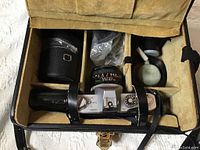 Open camera case showing Canon FTb camera with attached lens, two additional lenses, cleaning blower, small plastic bag, and leather lens case.