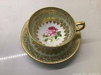 Close-up image of the interior of the cup showing the red rose pattern, gold leaf design, light blue background, and gold trim.