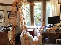 Assembled crane on wooden table with lattice boom vertical, crawler tracks in view, hook suspended