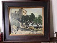 Frontal view of the framed oil painting showing the building, trees, and signature with a soda can for scale