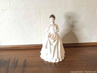 Full view of the Royal Doulton porcelain figurine depicting a woman in a white tiered dress with short brown hair.
