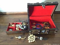 Wide view of the wooden jewellery box open showing the upper lid, red fabric lining, and various jewellery items including cufflinks and a decorative enamel box.