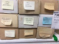 Photo of nine cardboard boxes labeled with baseball card set years and brands from early 1990s such as Leaf, Topps, Donruss, Flair and Score.