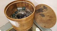 Photo of wooden barrel showing interior with assorted blue and clear canning jars inside.