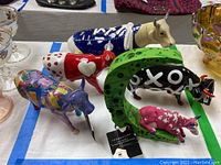 Top view of five Cow Parade figurines arranged on a table, showing various colorful painted designs and tags on some pieces.