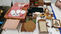 Full lot showing miniature dollhouse furniture including table, chairs, bed, dresser, sofa, bathtub, and sink pieces alongside baskets with tea set items.