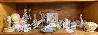 Shelf display showing multiple figurines and decorative plates, including swan figurine and various human shaped figures