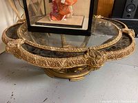 Full view of round glass top coffee table with gold ornate base and a display case on top (not included).
