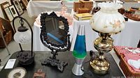 Photo showing all four items on table: cast iron lamp with kittens, black cast iron mirror, lava lamp, brass hurricane lamp
