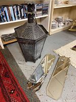 Metal Asian style lantern with hinged top, showing intricate cutout panels and weathered surface next to the beveled mirrors