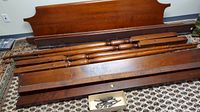 Disassembled mahogany four post bed components laid on patterned carpet, showing headboard, side rails, posts with finials, and hardware box.