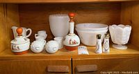 Full set of 14 milk glass pieces including bowls, salt and pepper shakers, decanter, and decorative pieces on wooden shelf