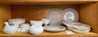 Shelf of various white milk glass items including hen on nest covered dish, hobnail bowls, scalloped edge plates, and divided gold trimmed dishes.