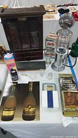 Overview of entire lot displayed on a table including Remy Martin wall cabinet, High Octane Alcohol dispenser, boxed liquor bottles and decanters, shot glasses, coasters, pipe, and flashlight box.