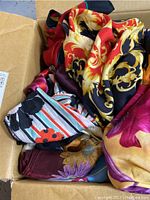 Open box showing several colorful scarves including a silk piece with ornate gold patterns on red and navy background, and others with floral and abstract designs.