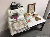 Singer 4830C sewing machine with purple thread spools, vintage linens, small boxes, and framed alphabet sampler print on a wooden table.