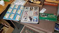 Photo showing the opened binder with mixed sports trading cards sleeved inside, including hockey and football cards. The sealed Score football card set box is also visible on the table.