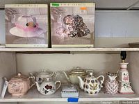 Photo of five vintage teapots, ceramic pineapple vase, ashtray holder with two ashtrays, and three lamps including UMA Classics boxed hat lamps