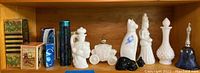 Photo shows variety of vintage Avon perfume bottles and collectibles arranged on a wooden shelf including milk glass pieces shaped like animals and figurines, as well as boxed items.