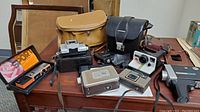 Wide view showing collection of vintage cameras and camera bags on wooden table