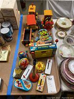 Overview of the lot showing vintage wooden train set, Fisher Price TV-Radio, colorful noise makers, and nearby dishware.