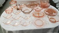 Overview of assorted pink depression glass on a white cloth—bowls, plates, candy dish, shakers visible