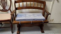 Front view of solid wood bench with trestle base and removable light blue tufted cushion on seat.