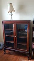 Wooden bookcase with two glass front doors, medium brown finish, and metal knobs, shown on hardwood floor