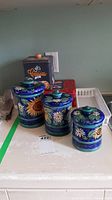 Photo showing three ceramic canisters with sunflower and daisy designs and two cookie tins, plus drawer tray underneath.