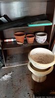 Shelf with small terracotta pots, ceramic floral pot, garden kneepad, and ground screening fabric
