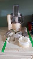 Image showing the Moulinex food processor base and bowl with clear lid along with assorted accessories including blades and plastic parts.