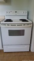 Front view of white Kenmore electric stove with four coil burners, control knobs, digital display, and oven door with window.