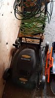 Top-down view showing Yardworks branded black lawn mower with green and yellow grass catcher bag and coiled electric cords on handle.