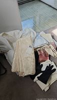 Large cream-colored damask floral table cloths with leather gloves and satin scarf on the floor.